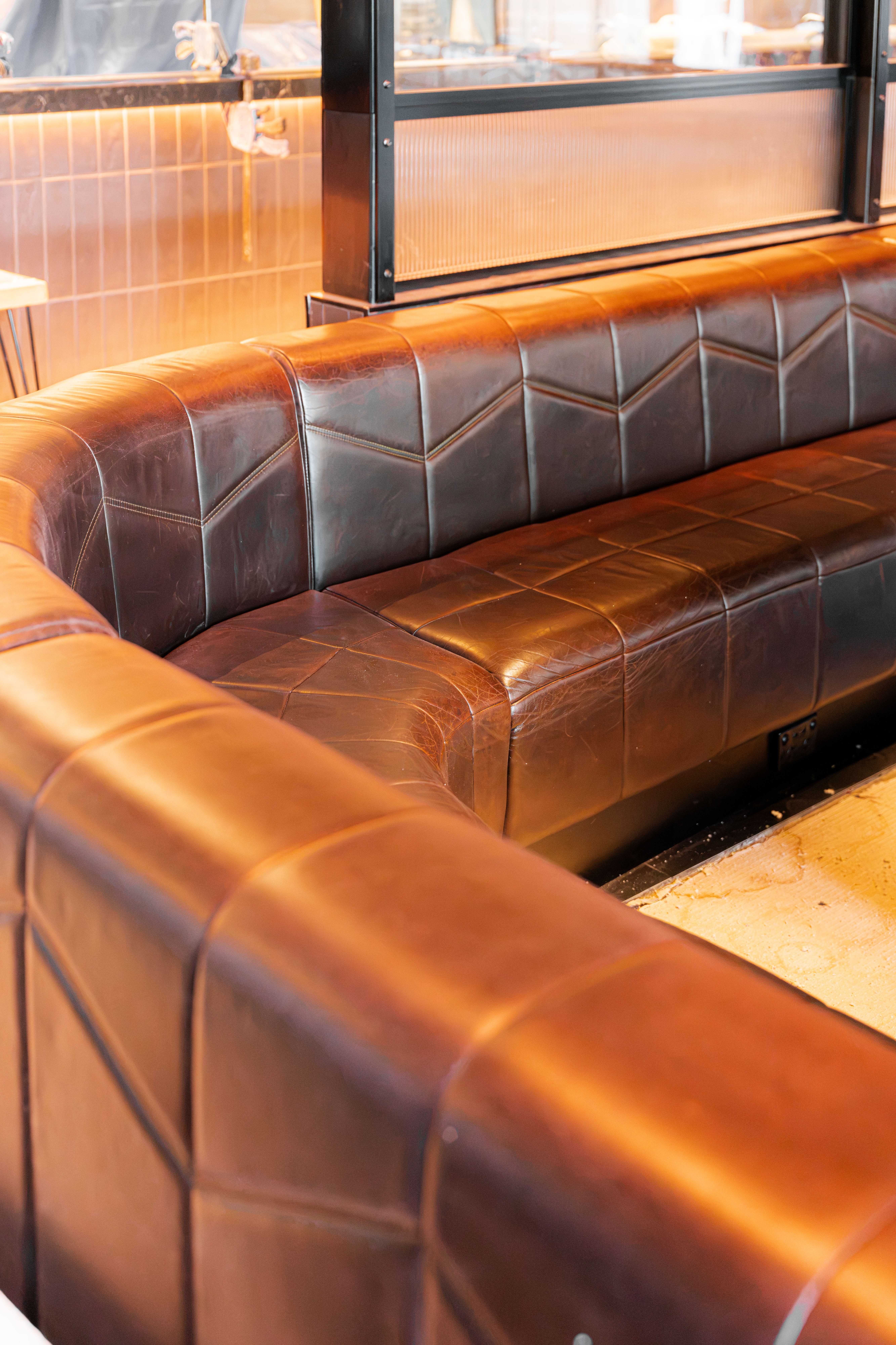 Restored dark cognac leather banquette with chevron stitched back panels in a restaurant, photographed after an overnight restoration with the venue set to trade