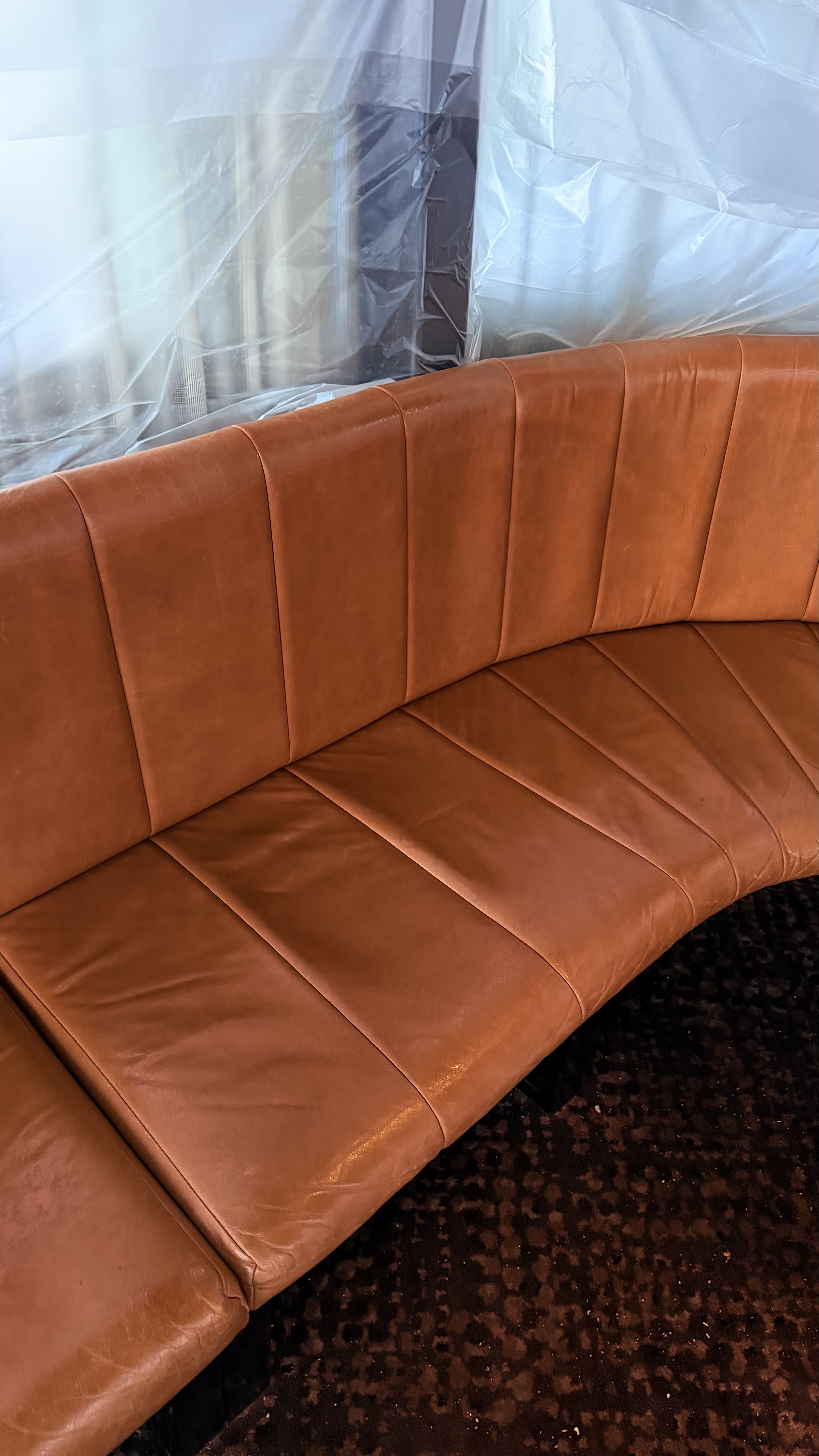 Caramel leather curved banquette fully restored inside a venue, with plastic sheeting still masking the fittings behind it from the overnight shift
