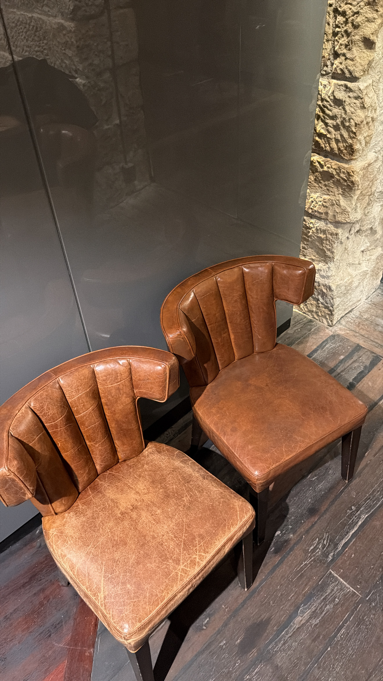 Two tan leather channel back dining chairs side by side on a venue floor, the left one cracked and faded before restoration, the right one restored to an even finish