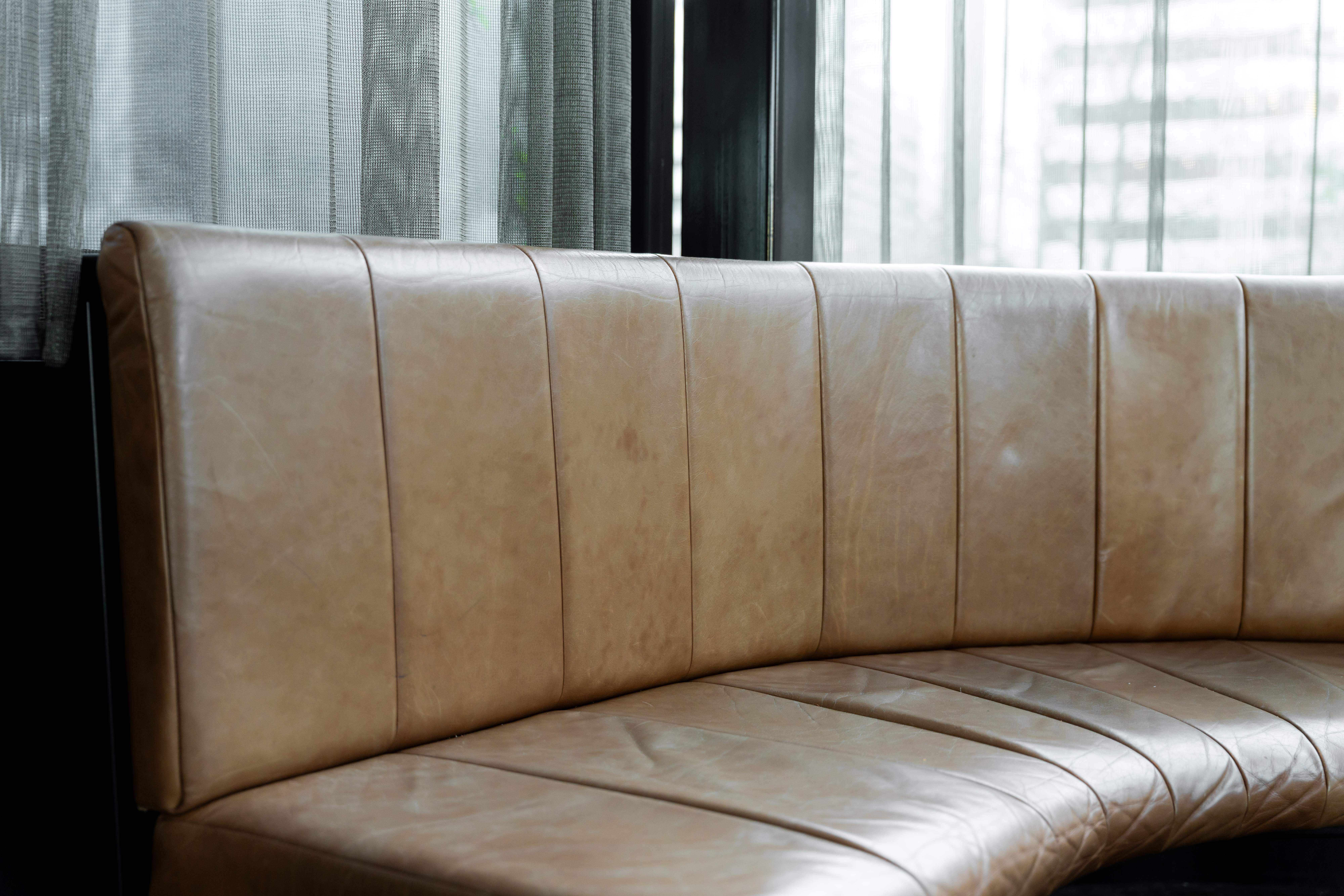 Tan leather channel back banquette along a window in a venue, restored and conditioned, the grain even across every panel