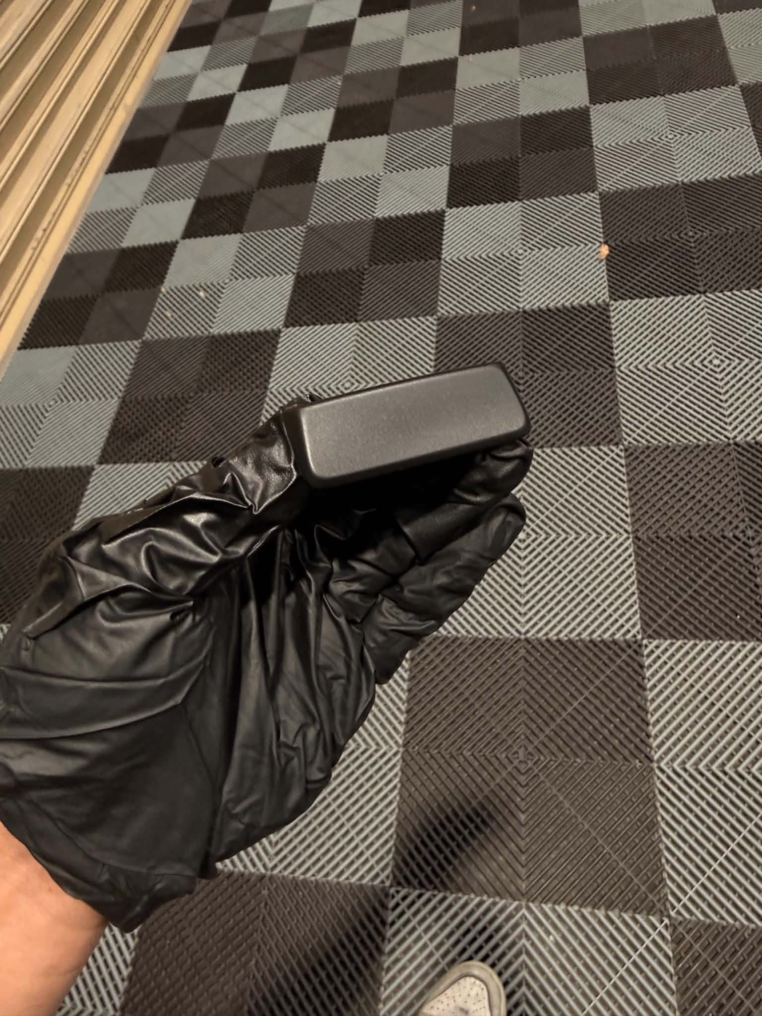The same button recoated in fresh black, held in a gloved hand, ready for the symbol to be laser etched back through to the white core