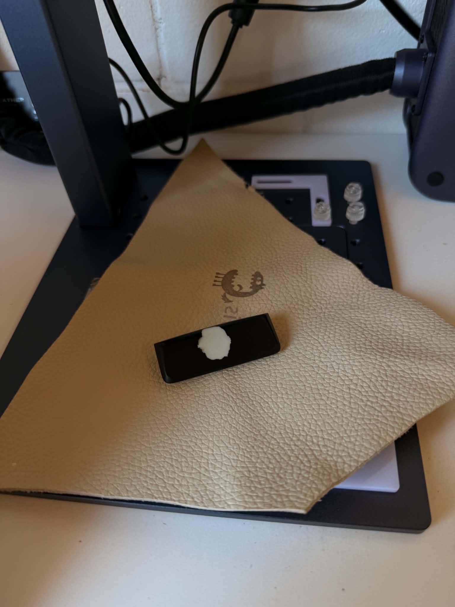 Example of a failed button coating: the black soft touch layer has lifted and torn away in a patch, exposing the white plastic underneath, photographed on the laser bed before restoration
