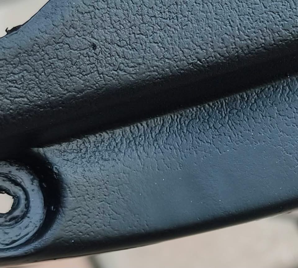 Close up of a repaired black plastic trim piece with laser regrained texture running continuously across the repair and around the mounting hole, no smooth patch visible
